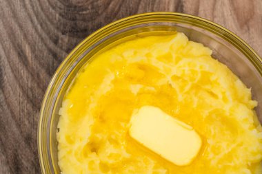 Erimiş tereyağlı ezilmiş patates, ahşap arka planda cam bir kaseye yakın.