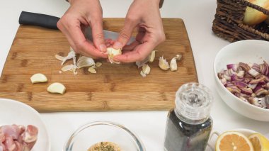 Tahta kesme tahtasına sarımsak soyuyorlar, beyaz mutfak masasına yaklaşıyorlar, kadın elleri, yukarıdan manzara.