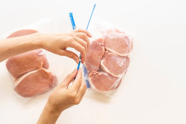 Raw boneless pork loin chops in zip lock bags. Woman packs meat in bags, close up view, white background, directly from above
