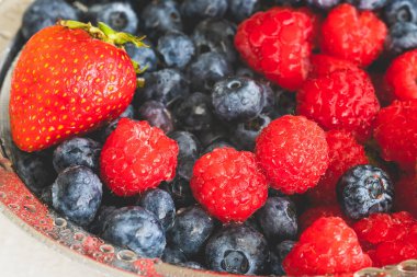 Taze olgun yıkanmış çilek, yabanmersini, ahududu kevgire yakın beyaz arka planda.