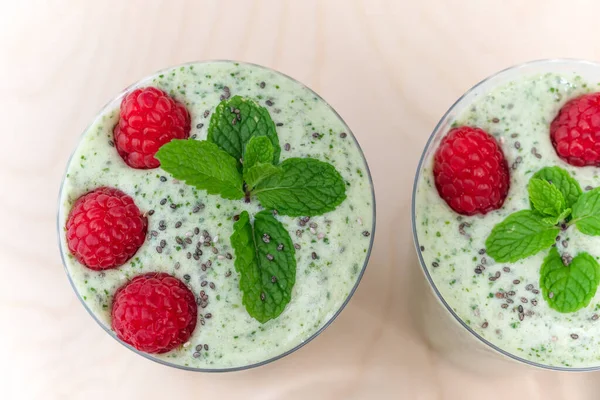 Celery banana smoothie with mint and fresh raspberries in glasses close up on wooden background, view from above