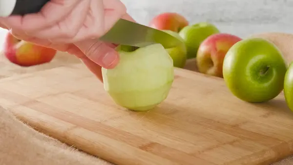Woman hands cut apples on a wooden cutting board close-up on a kitchen table