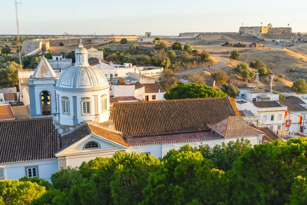 Igreja Matriz de Castro Marim 'in önde gelen kubbesi arka planda tarihi tepe kalesiyle çatılar arasında yükseliyor..