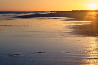 Altın gün batımı plaj boyunca takip eden ıslak kumda yansıyor..