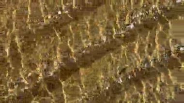 Dalgalanan temiz su, küçük çakıl taşları üzerinde altın desenler yaratır. Yüksek kalite 4k görüntü