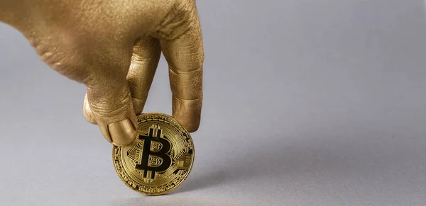 Golden hand holds physical coin of cryptocurrency bitcoin.