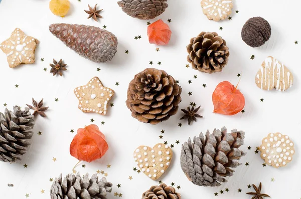 Helles weihnachtliches Layout mit Lebkuchen, Tannenzapfen und orangefarbenen Physalis auf einem weißen Holztisch. — Stockfoto