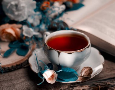 Eski bir porselen çay bardağı, taze küçük gül, salyangoz ve kitap ile Vintage hala hayat.