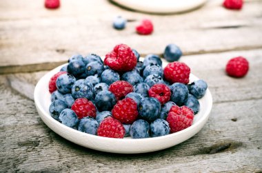 Bahçede, eski bir tahta masada yaban mersini ve ahududu ile natürmort. Kırsal doğal gıda tarzı.