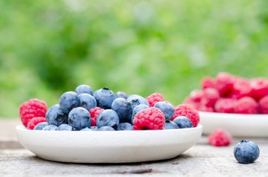 Bahçede, eski bir tahta masada yaban mersini ve ahududu ile natürmort. Kırsal doğal gıda tarzı.