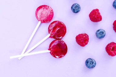 Kırmızı Lolipop, Yaban Mersini ve Ahududu Bir Mor Renk Arka Plan. ÜstTen Görünüm Düz Döşeme Arka Plan.