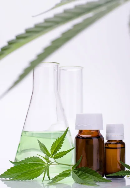 Fondo médico, tema químico con hojas de cannabis, botella de aceite y frascos de vidrio de laboratorio detrás en un blanco . — Foto de Stock