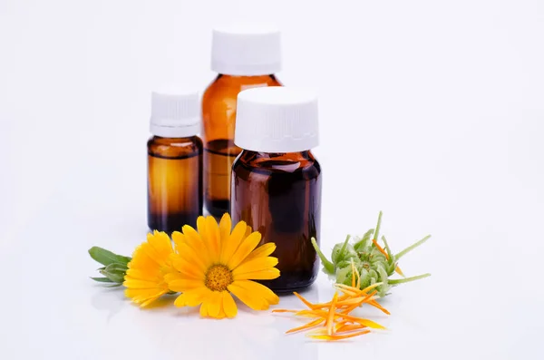 Dark cosmetic bottle of aromatic oil for herbal medicine with calendula flower isolated on white backdrop. Marigold extract. — Stock Photo, Image