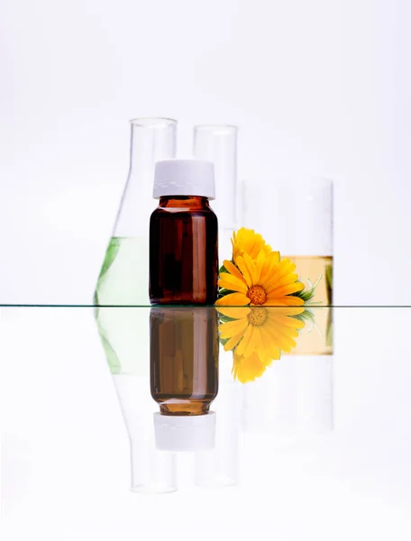 Dark cosmetic bottle of aromatic oil for herbal medicine with calendula flower isolated on white backdrop. Marigold extract. — Stock Photo, Image