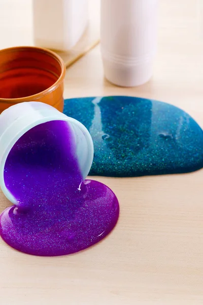 Haciendo limo tú mismo. Ingredientes para hacer limo brillante brillante en casa. El limo violeta se derrama en una mesa del recipiente de plástico . — Foto de Stock