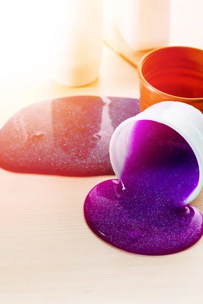 Faire de la boue toi-même. Ingrédients pour faire de la boue brillante scintillante à la maison. Violet déversements de boue sur une table à partir d'un récipient en plastique . — Photo