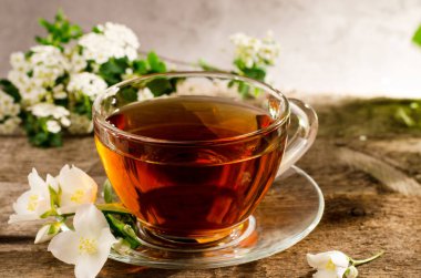 Yasemin çiçekli güzel kokulu çay. Eski ahşap bir masada cam çay fincanı. Fililadelphus çiçekli sıcak içecek.