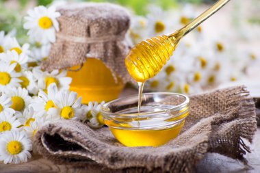 Kavanozda tatlı bahar bitkisel balı ve ballı küçük cam kase. Masanın üzerinde taze papatya çiçekleriyle aromatik bal bileşimi.