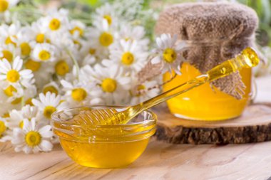 Kavanozda tatlı bahar bitkisel balı ve ballı küçük cam kase. Masanın üzerinde taze papatya çiçekleriyle aromatik bal bileşimi.