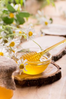 Kavanozda tatlı bahar bitkisel balı ve ballı küçük cam kase. Masanın üzerinde taze papatya çiçekleriyle aromatik bal bileşimi.