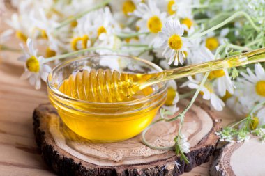 Kavanozda tatlı bahar bitkisel balı ve ballı küçük cam kase. Masanın üzerinde taze papatya çiçekleriyle aromatik bal bileşimi.