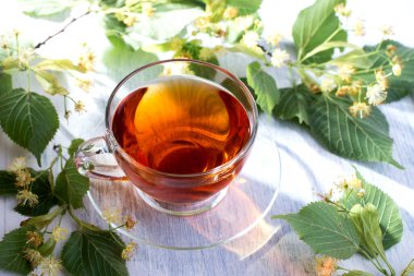 Bir bardak ıhlamur çayı ve beyaz ahşap bir masada ıhlamur çiçeği. Sağlık hizmeti sıcak içeceği.