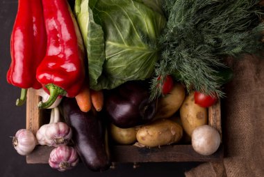 Tahta bir kutuda siyah arka planda taze çiğ sebzeler. Sağlıklı organik yerel yiyecekler.