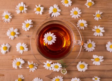 Tahta bir masada papatya çiçekli bir fincan sıcak bitki çayı. Sabah kahvaltısı teması.