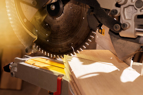 Carpenter working with power circular miter to cut wooden board against dark background.