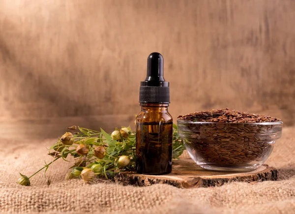 Flaxseed oil cosmetic bottle. Composition with dispenser bottle, flax seeds, and plants on sackcloth.