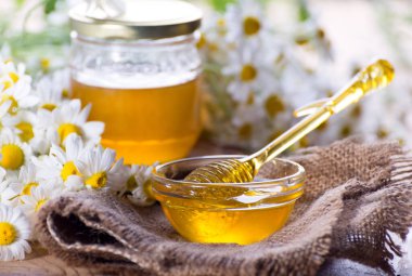 Kavanozda tatlı bahar bitkisel balı ve ballı küçük cam kase. Masanın üzerinde taze papatya çiçekleriyle aromatik bal bileşimi.