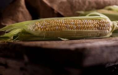 Eski ahşap bir masada taze çiğ mısır. Sonbahar hasadı hala karanlık bir ruh hali içinde..