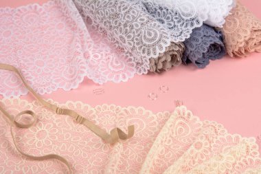 Roll of Delicate color laces for panties and bras on pink background with plastic fittings. Elastic material. Using for Atelier and fabric store.