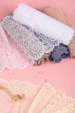 Roll of Delicate color laces for panties and bras on pink background with plastic fittings. Elastic material. Using for Atelier and fabric store.