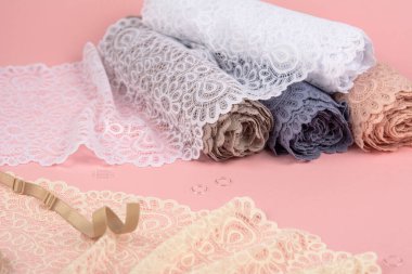 Roll of Delicate color laces for panties and bras on pink background with plastic fittings. Elastic material. Using for Atelier and fabric store.