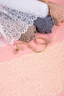 Roll of Delicate color laces for panties and bras on pink background with plastic fittings. Elastic material. Using for Atelier and fabric store.