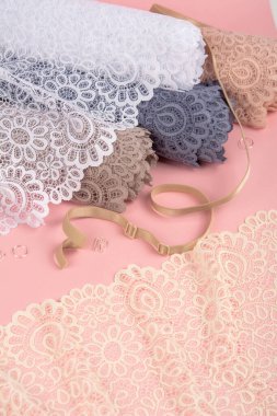 Roll of Delicate color laces for panties and bras on pink background with plastic fittings. Elastic material. Using for Atelier and fabric store.