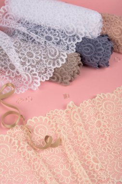 Roll of Delicate color laces for panties and bras on pink background with plastic fittings. Elastic material. Using for Atelier and fabric store.