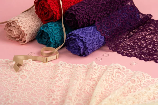 Roll of Delicate color laces for panties and bras on pink background with plastic fittings. Elastic material. Using for Atelier and fabric store.