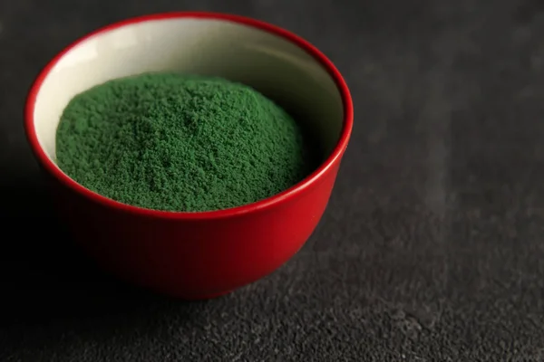 red bowl with Heap of green chlorella or spirulina algae, or matcha, on gray concrete background. Superfood concept powder. Space for text.