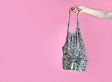 Kadının elinde gri örgü bir ip torbası var, içinde teneke kutular, insani yardım, gıda bağışı, pembe arka planda. Metin için boşluk