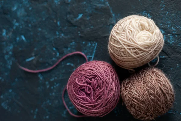 three beige pink brown Color balls skein of wool yarn for crochet and knit on dark blue texture putty concrete. Flatlay image with space for text.