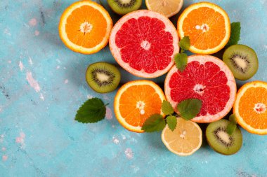 Portakal, limon, greyfurt ve naneli kivi meyvesi ve mavi beton arka planda. Düz görünüm, metin için boşluk.