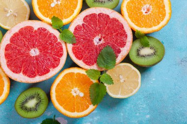 Portakal, limon, greyfurt ve naneli kivi meyvesi ve mavi beton arka planda. Düz görünüm, metin için boşluk.