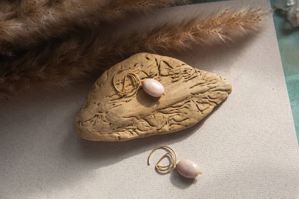 Stylish earrings made natural pink opal stone with Golden brass fittings piece of wood pattern from activity bark beetle. Natural day solar lighting. — Stock Image Stylish Earrings Made Natural Pink Opal Stone Golden Brass Fittings Stock Picture
