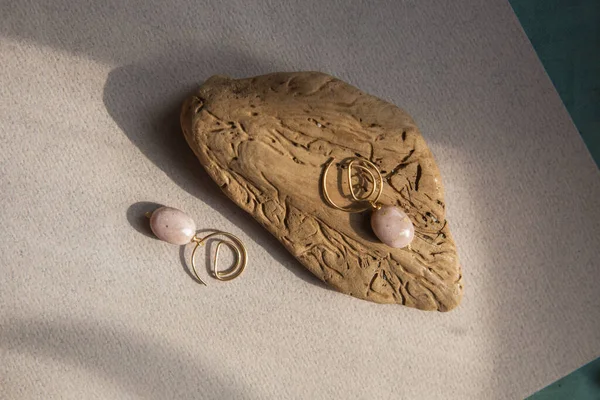 Stylish earrings made natural pink opal stone with Golden brass fittings piece of wood pattern from activity bark beetle. Natural day solar lighting. — Stock Image Stylish Earrings Made Natural Pink Opal Stone Golden Brass Fittings Royalty Free Stock Images