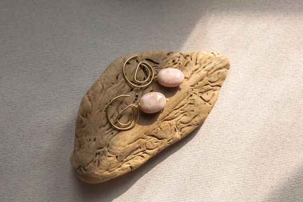 Stylish earrings made natural pink opal stone with Golden brass fittings piece of wood pattern from activity bark beetle. Natural day solar lighting. — Stock Image Stylish Earrings Made Natural Pink Opal Stone Golden Brass Fittings Stock Photo