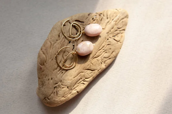 Stylish earrings made natural pink opal stone with Golden brass fittings piece of wood pattern from activity bark beetle. Natural day solar lighting. — Stock Image Stylish Earrings Made Natural Pink Opal Stone Golden Brass Fittings Royalty Free Stock Images