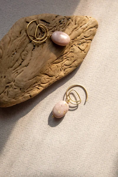 Stylish earrings made natural pink opal stone with Golden brass fittings piece of wood pattern from activity bark beetle. Natural day solar lighting. — Stock Image Stylish Earrings Made Natural Pink Opal Stone Golden Brass Fittings Stock Picture