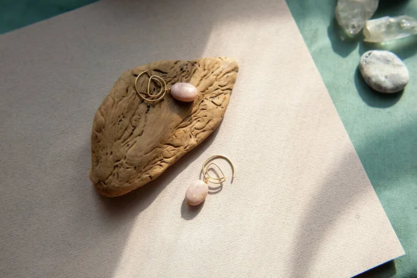 Stylish earrings made natural pink opal stone with Golden brass fittings piece of wood pattern from activity bark beetle. Natural day solar lighting. — Stock Image Stylish Earrings Made Natural Pink Opal Stone Golden Brass Fittings Stock Image